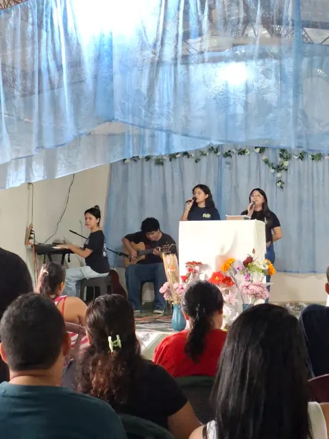 Jóvenes cantando y tocando guitarra y teclado frente a la congregación.