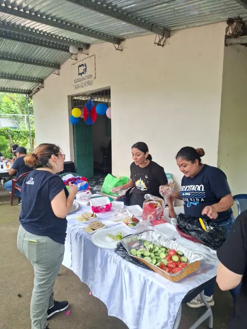 Voluntarios preparando almuerzo y refrigerios sobre una mesa junto al templo.