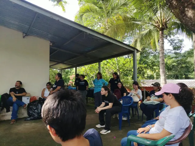 Grupo de personas sentadas y reunidas bajo un área techada al aire libre.