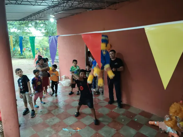 Niños y colaboradores participando en un juego de piñata bajo un techo decorado.