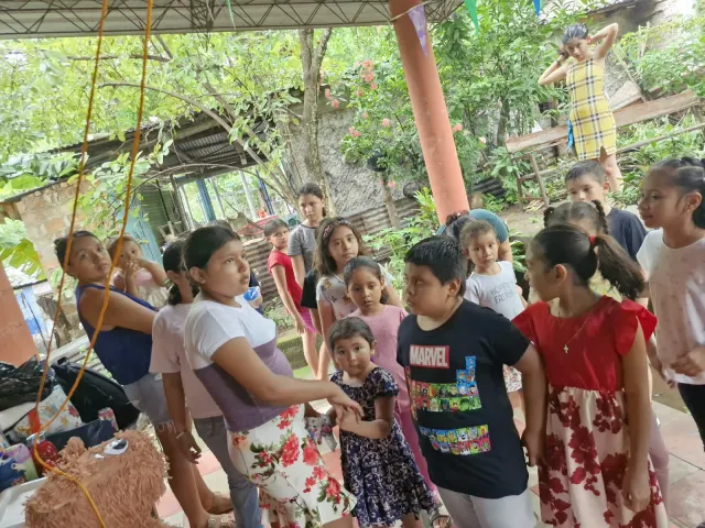 Grupo de niños reunidos bajo un techo decorado con banderines, cerca de una piñata.